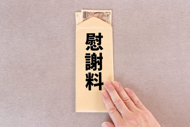 1万円札が多く入った「慰謝料」と書かれた茶色の封筒を右手で差し出す